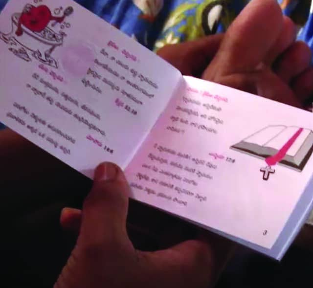 A person's hands are holding a small gospel tract. The left side of the booklet displays text, accompanied by a graphic of a heart in a bathtub. The right side contains more text with an illustration of an open Bible with a pink ribbon bookmark and a Christian cross, indicative of the tract's religious message. The specific text is indistinct.