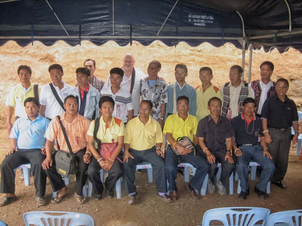A group photo of first, second, and third generation Akha preachers with Jon, smiling for a photo under a shaded area in Thailand.