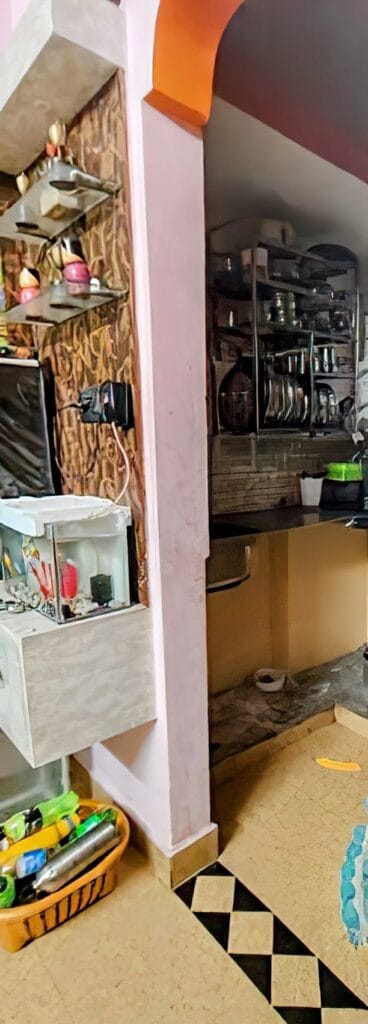 Inside a small, multifunctional kitchen in a tiny house located in a slum area of Bengaluru, where cooking, dishwashing, and bathing spaces converge in a testament to the family's adaptability.