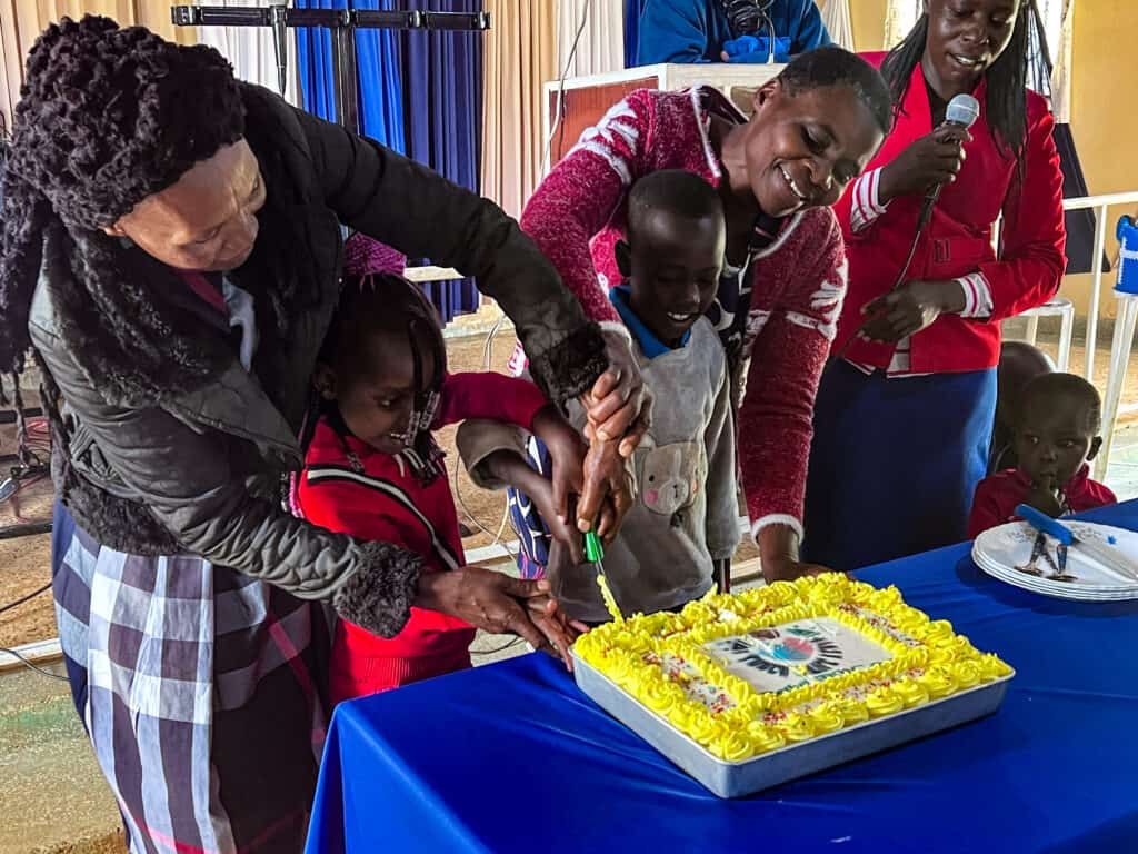 Joyful children and adults gather around a cake at a celebration event, ready to share a special moment together.