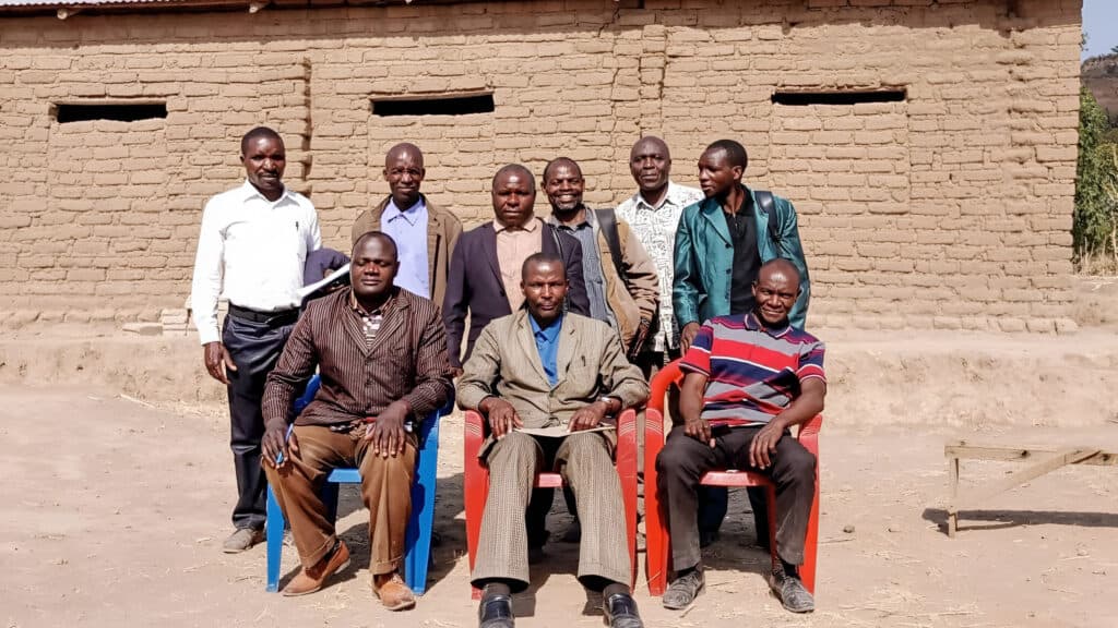 A group of dedicated church planters posing for a photo in front of a mud brick building, representing the growth of their mission.