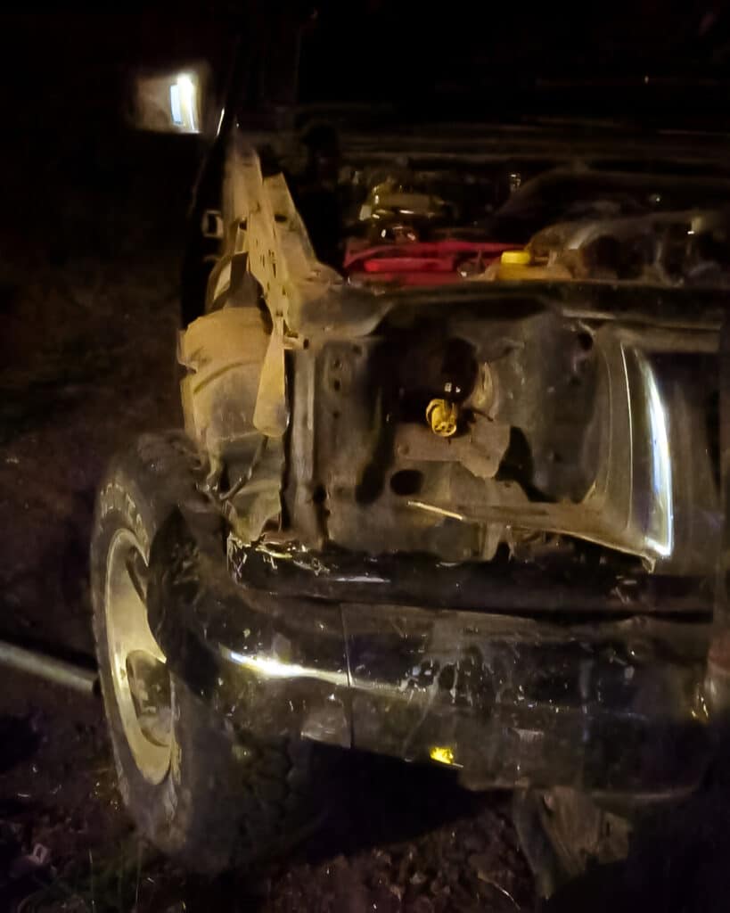 A damaged truck at night, with its hood open and front end visibly crumpled, indicative of a recent accident.