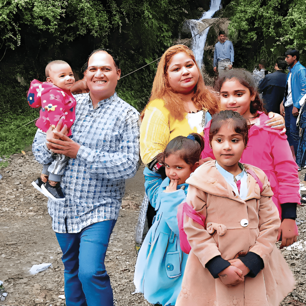 Shaukut, Mewish, and  family pose for a photo outdoors with a waterfall in the background, capturing a moment of joy and togetherness.