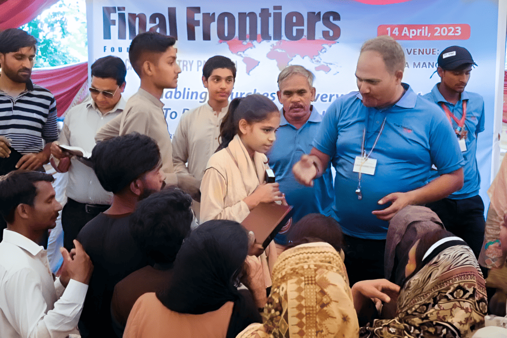A young participant confidently steps forward during a group activity at a youth camp, with attentive peers and adult mentors surrounding her, under a banner of Final Frontiers Foundation dated 14 April 2023.