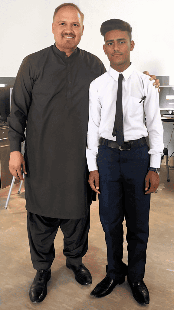 Two individuals, one in traditional black attire and the other in a smart white shirt and tie, stand side by side in a classroom, symbolizing mentorship and progress.