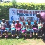 Children seated outside preparing to eat the food from our Touch A Life program before they attend their Sunday school lesson