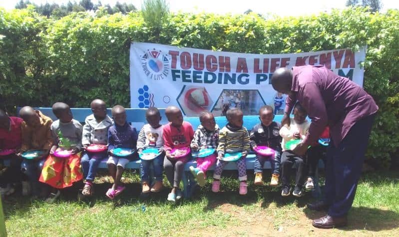 Children seated outside preparing to eat the food from our Touch A Life program before they attend their Sunday school lesson