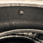 A close-up view of a worn tire with a distinct hole, showcasing its weathered texture and layers.