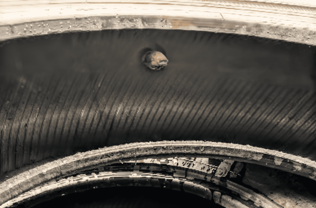 A close-up view of a worn tire with a distinct hole, showcasing its weathered texture and layers.