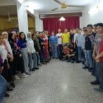 A meeting of the young teenage orphans from the earthquake, over 20 in total, in a building with white wall and red curtain in the background.