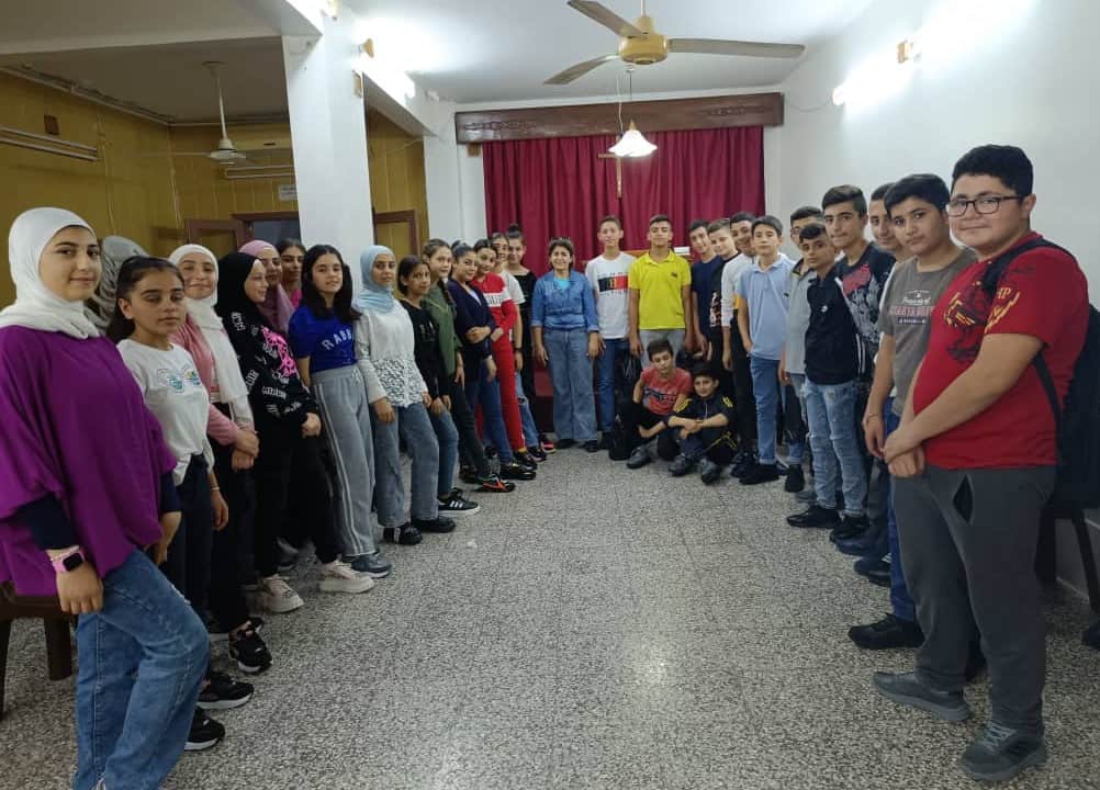 A meeting of the young teenage orphans from the earthquake, over 20 in total, in a building with white wall and red curtain in the background.