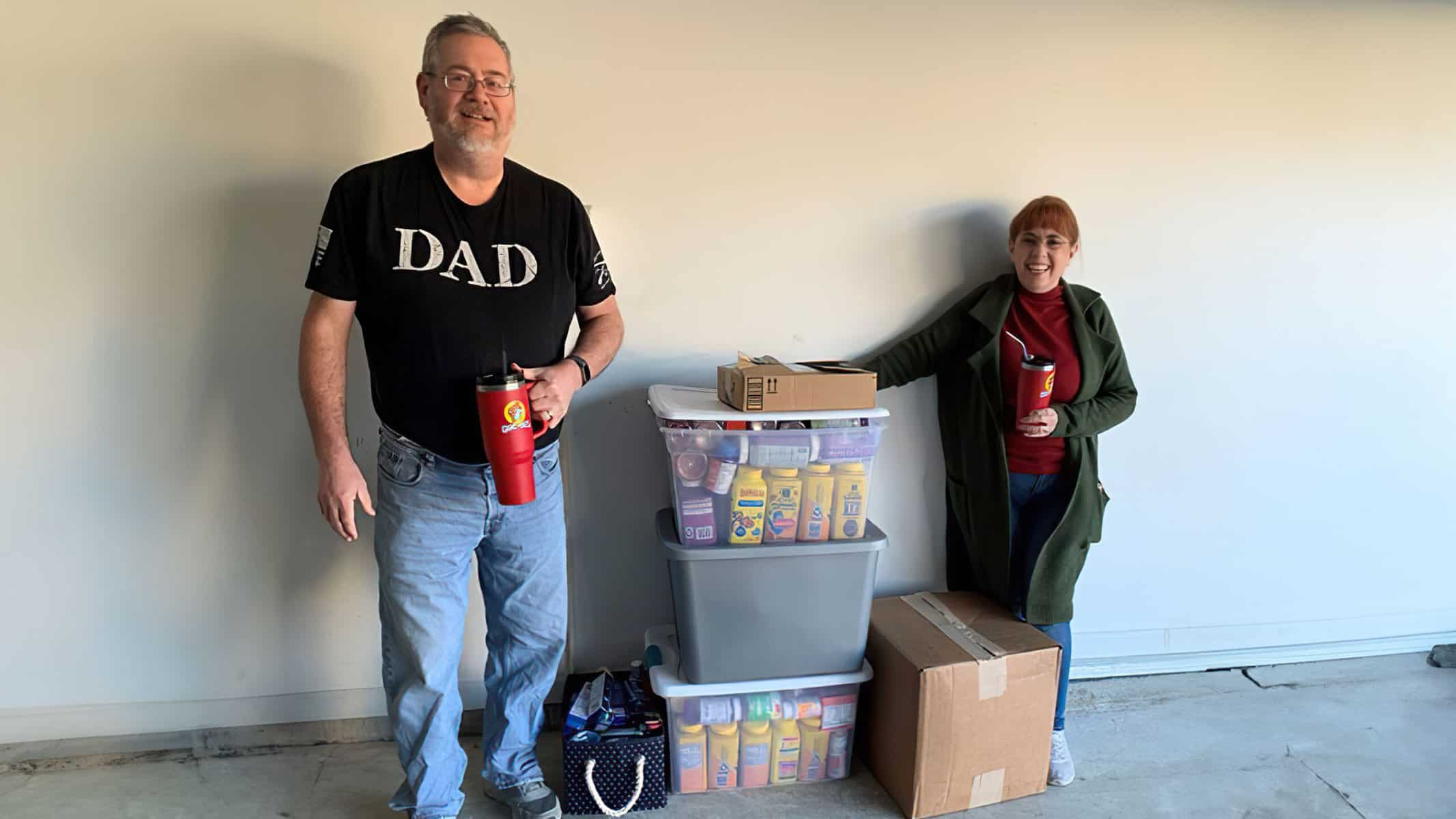 Dale and Cindee Dupaquier standing proudly in a garage next to a large storage bin and boxes filled with vitamin bottles for children in need.