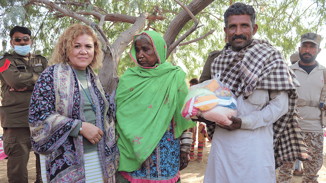 Nolin, a Christian missionary, stands with a Marwari couple receiving a food bag, flanked by a police officer and a volunteer military member from the church who now serves as security for the Bible College in Pakistan.