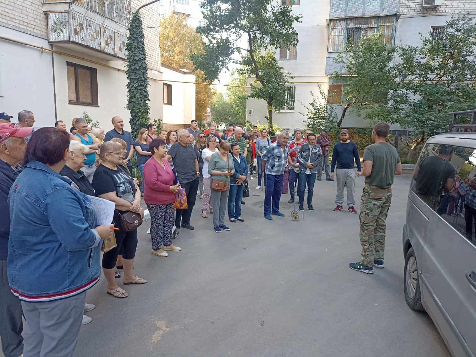 A group of people have gathered outside and are listing to a person preach a message. They are to receive food and a Bible.