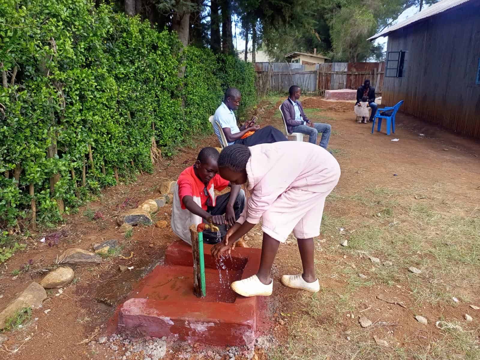Two people in Kenya using water from a faucet that is run from the new well.