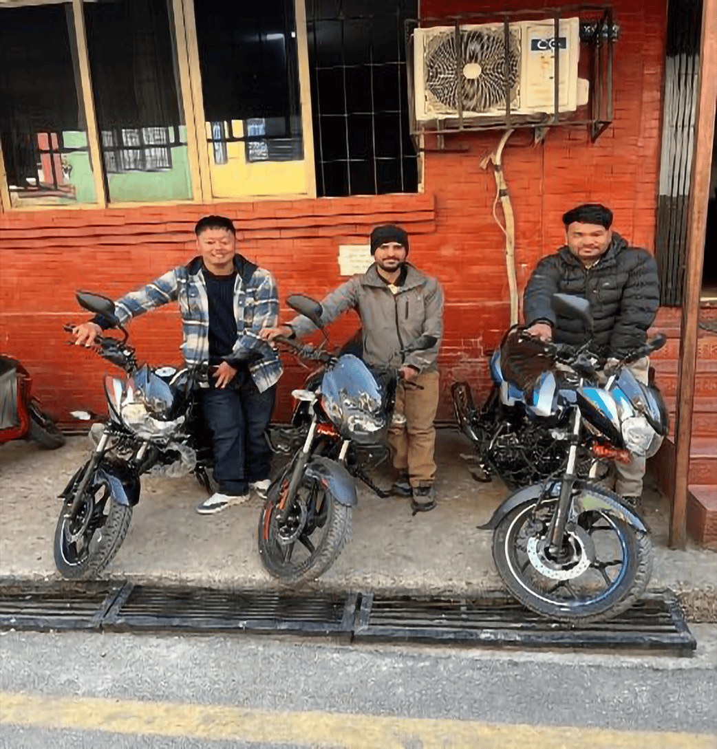 Three men stand next to their new motorcycles outside of a brick building in Nepal