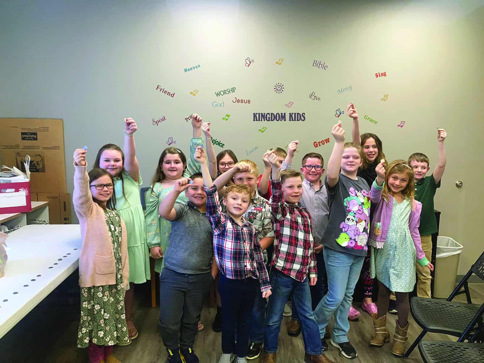 A group of children posing for a picture in a room. Each child is holding a coin.