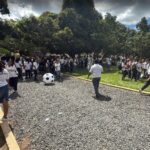 Students gathered outdoors at a school, preparing for a soccer activity under the shade of trees.