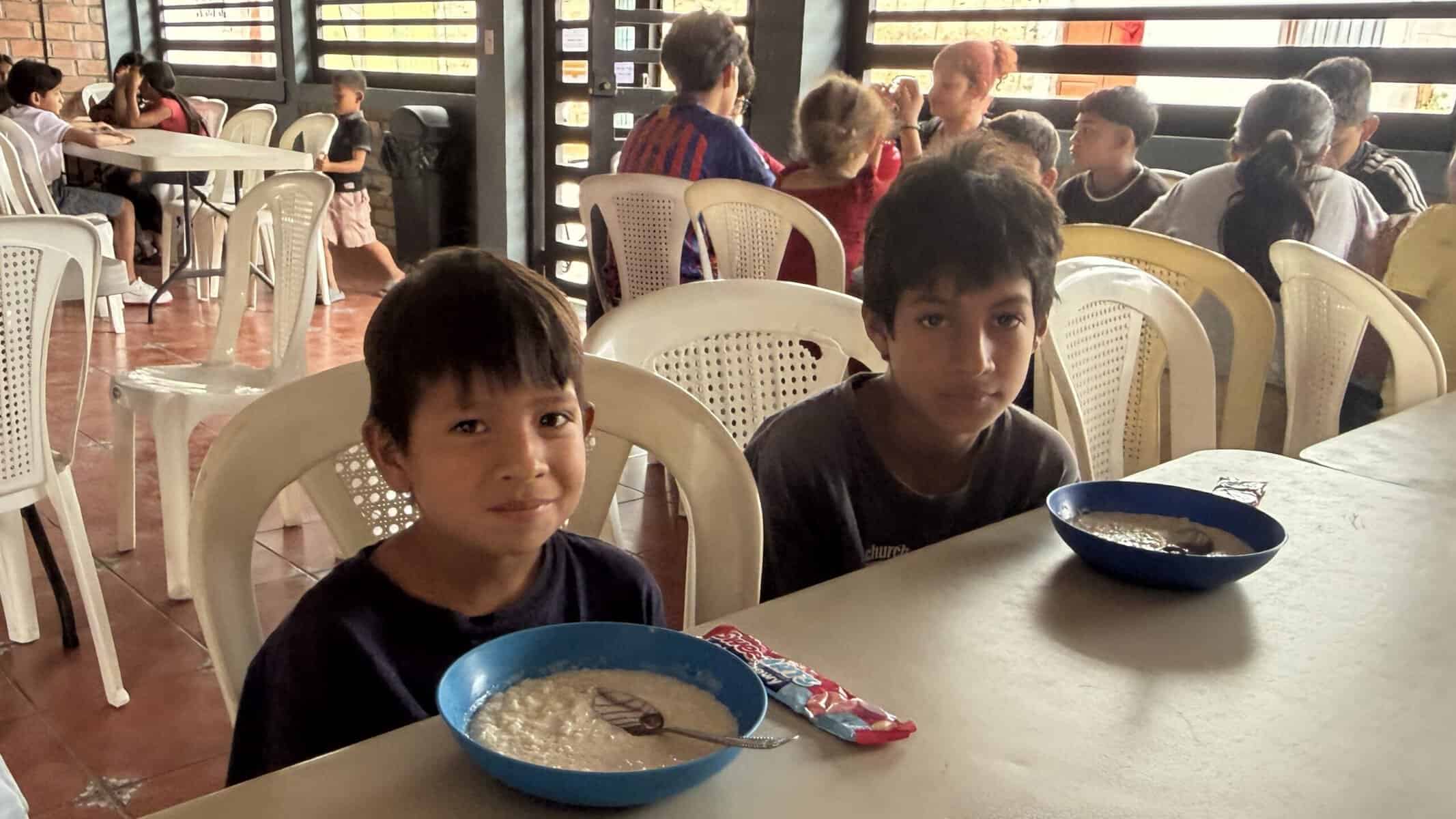 Two boys, 8 and 10 years old, sitting at a table, each with a bowl or arroz con leche.