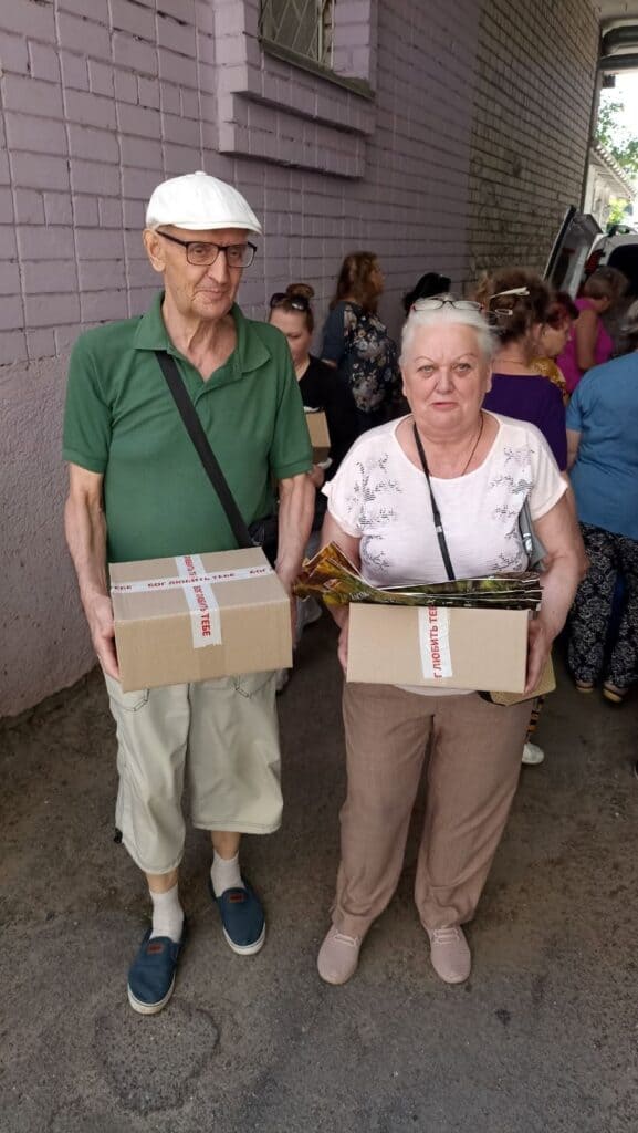 An elderly man and woman hold humanitarian aid boxes they received