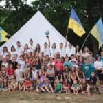 A large group of children and leaders with Ukrainian flags in front of a white tent